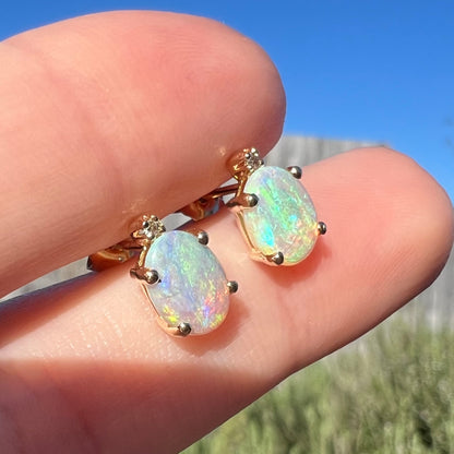 Angled close-up sunlit view of a pair of Australian crystal opal and diamond stud earrings in gold with green-blue color play.