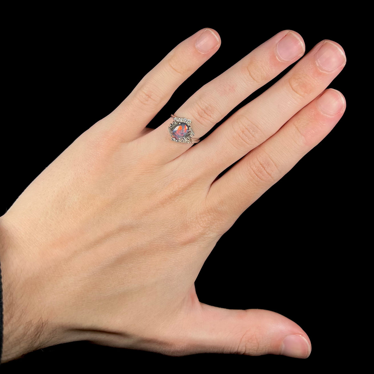 Hand wearing an Australian dark opal engagement ring with hexagonal diamond halo.  Red flashes are seen in the N5 opal.
