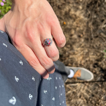 Close-up of person's hand resting on hip in sunlight wearing an Australian dark opal ring.  Vibrant red and orange flashes of color are seen in the opal.