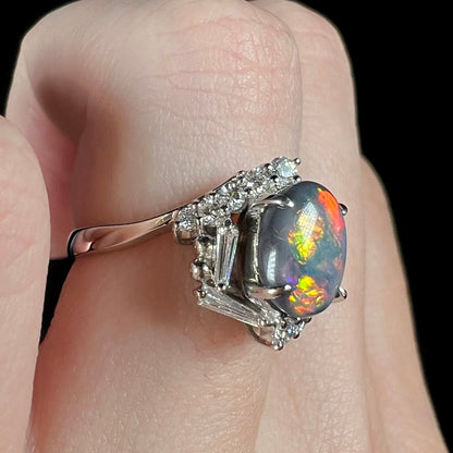 Side macro view of Australian dark opal ring with yellow, green, and red flashes of color showing under cool LED studio lights, worn on finger.