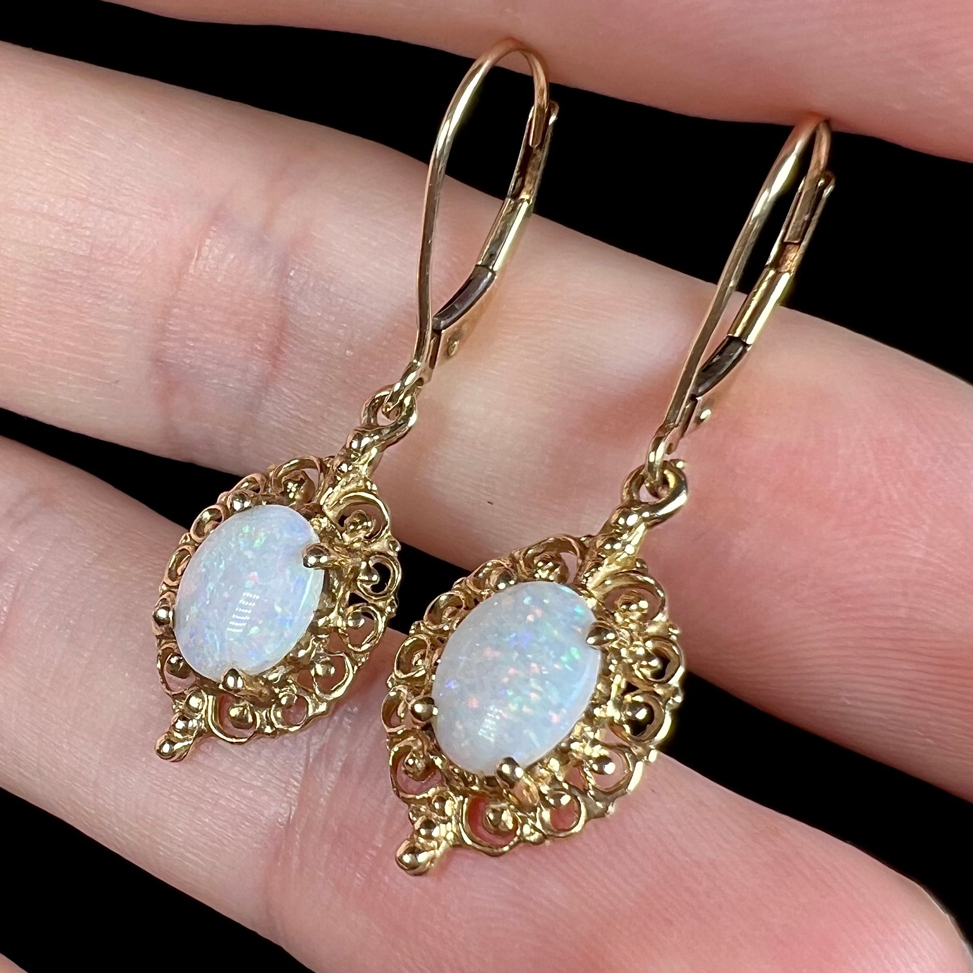 Angled close-up of a pair of vintage yellow gold Australian light opal dangle earrings shown in a hand.