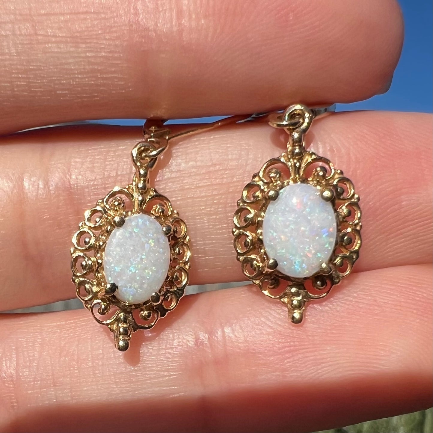 Close-up sunlit view of a pair of vintage yellow gold Australian light opal dangle earrings shown in a hand.