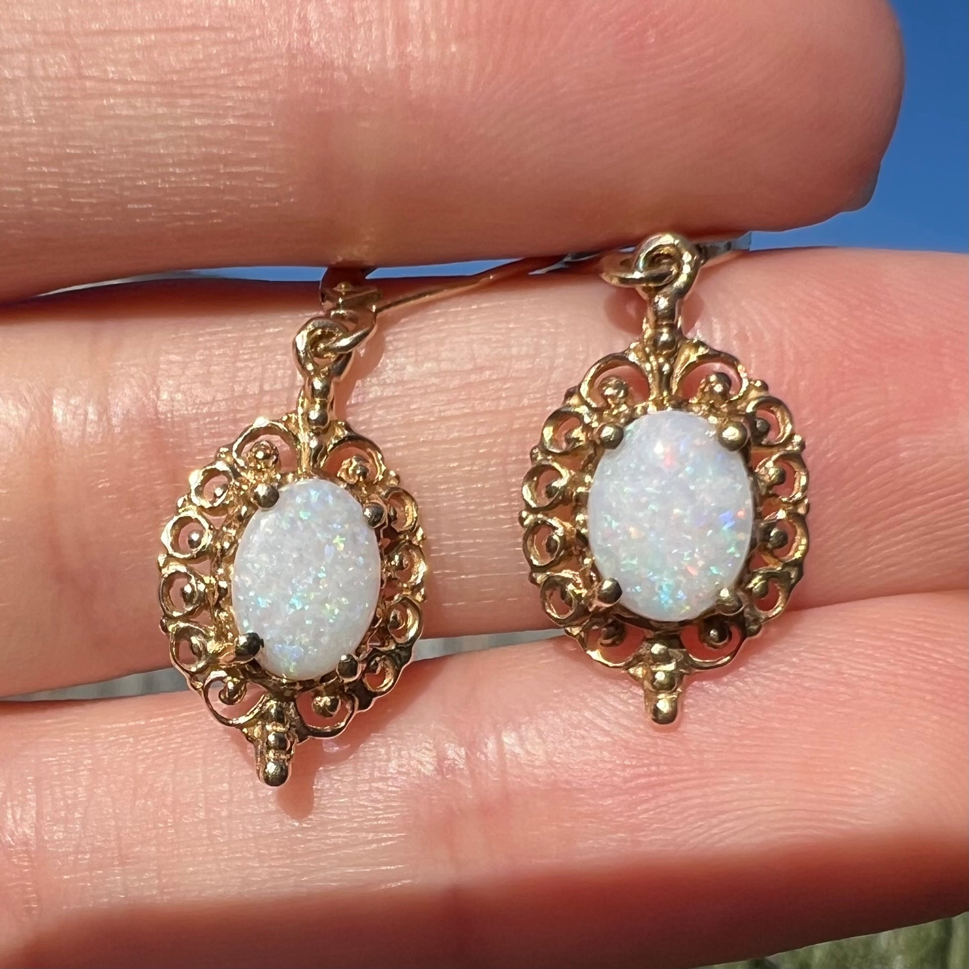 Close-up sunlit view of a pair of vintage yellow gold Australian light opal dangle earrings shown in a hand.