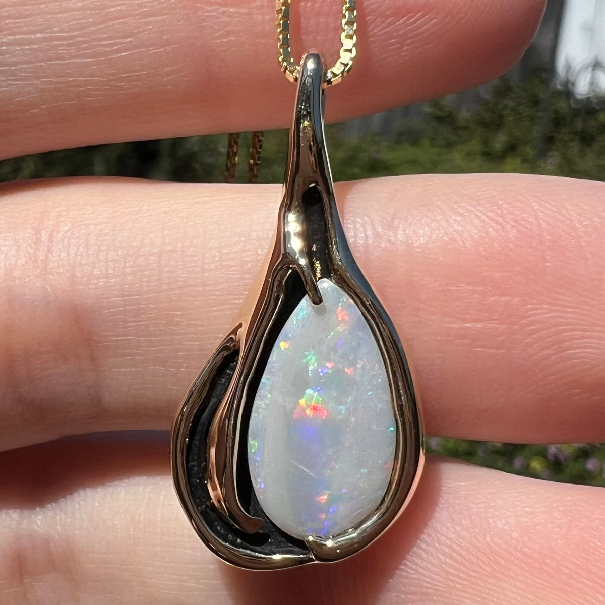 Close-up of Australian opal pendant with N7 light body in gold Modernist setting, shown under natural sunlight in hand
