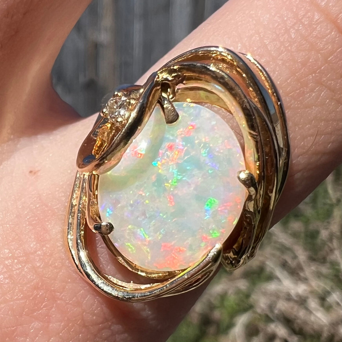 Close-up of Australian opal cocktail ring with swirling 14k gold design and diamond accent, worn on hand in natural light