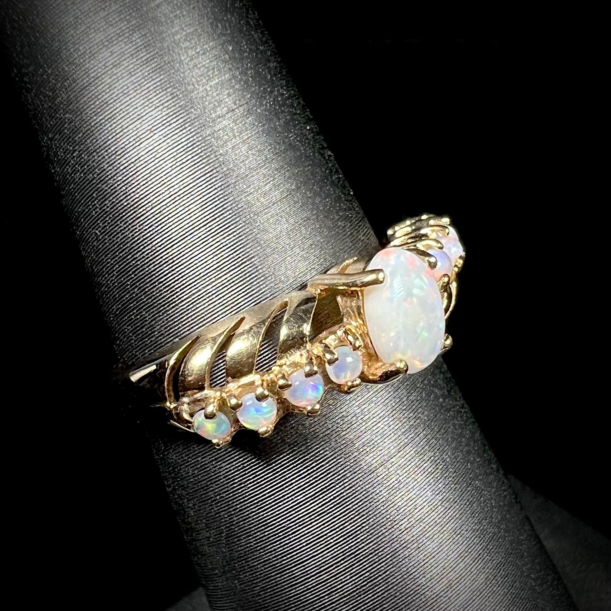 Angled view of an Australian white opal crisscross ring in yellow gold, shown on a ring display.