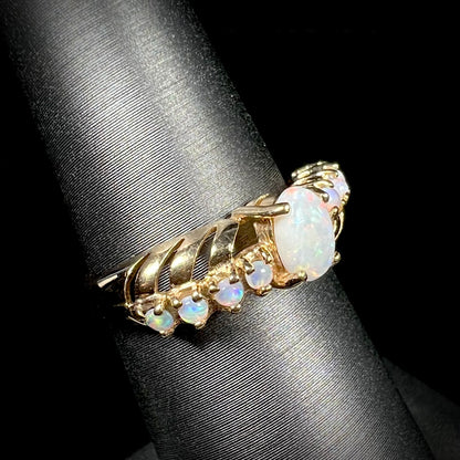 Angled view of an Australian white opal crisscross ring in yellow gold, shown on a ring display.