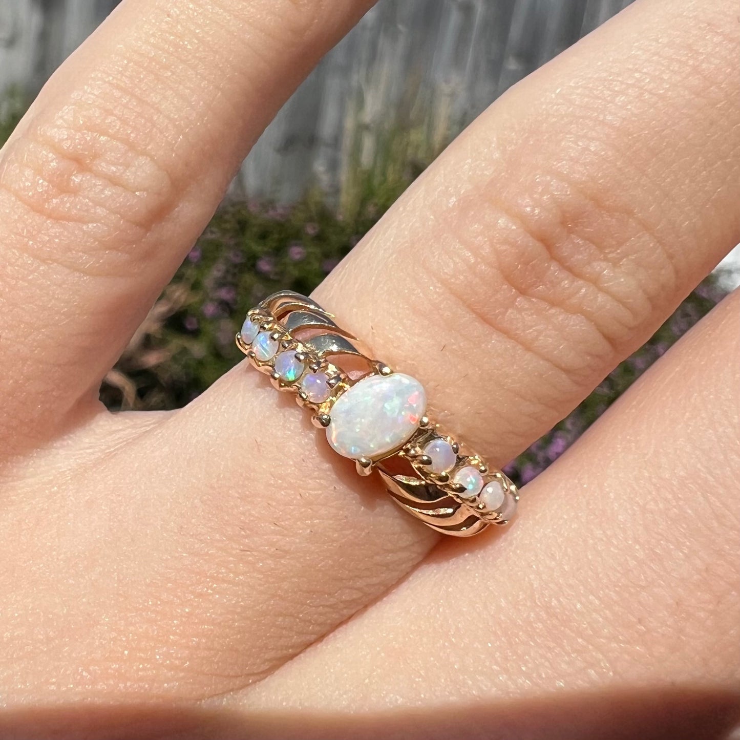 Close-up sunlit view of an Australian opal crisscross ring in yellow gold, worn on a finger.