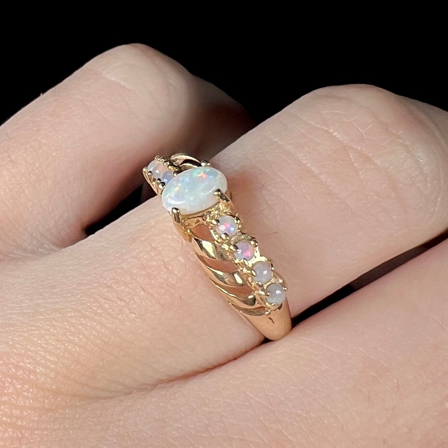 Angled close-up of an Australian opal crisscross ring in yellow gold, shown on a finger.