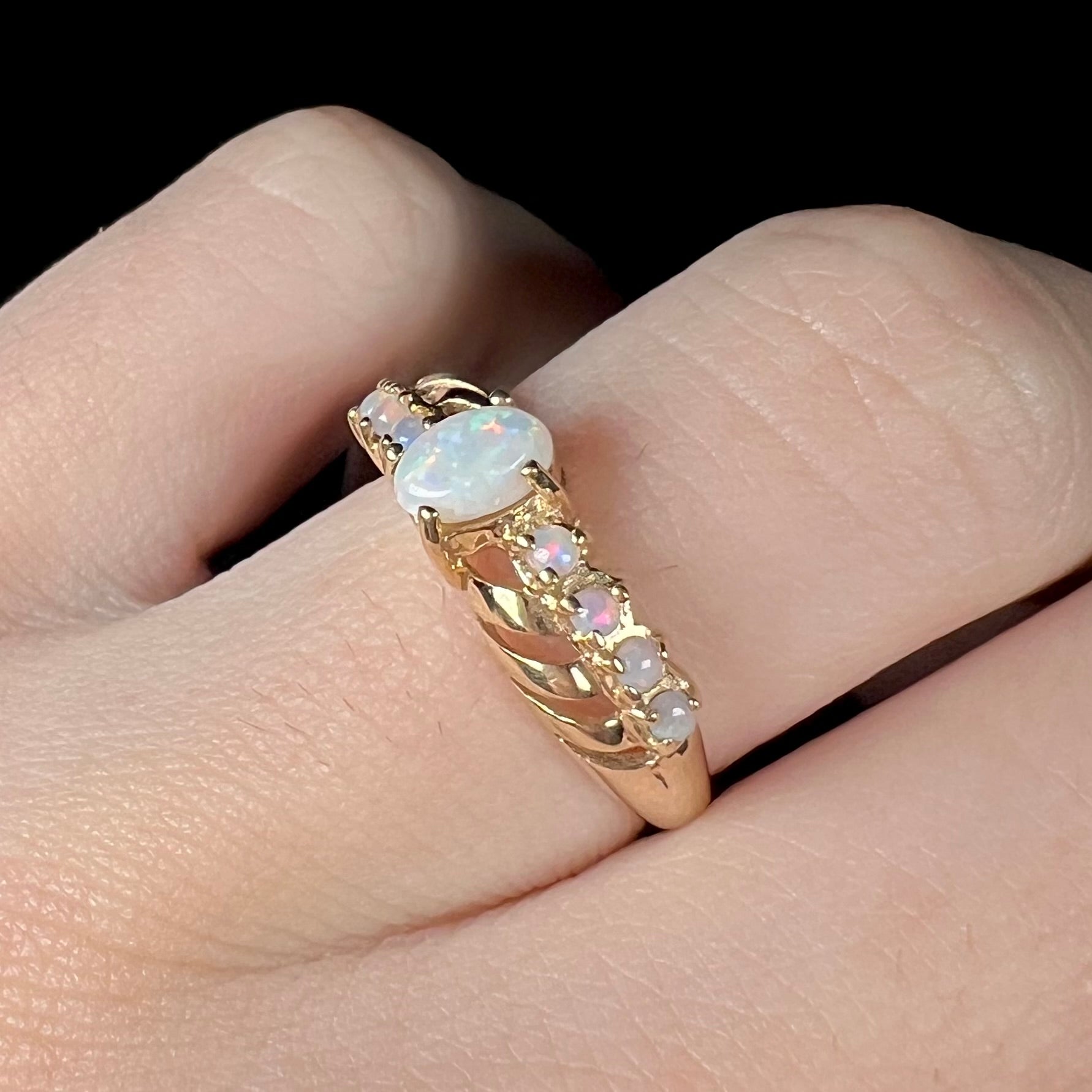 Angled close-up of an Australian opal crisscross ring in yellow gold, shown on a finger.