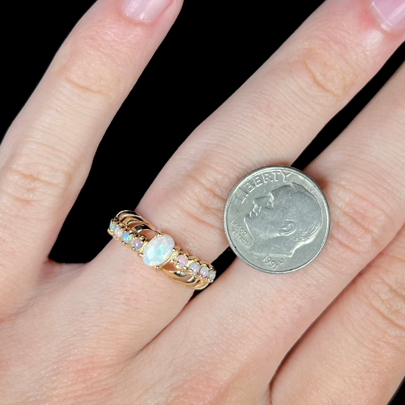 A yellow gold Australian opal crisscross ring, worn on a finger next to a dime coin for scale.