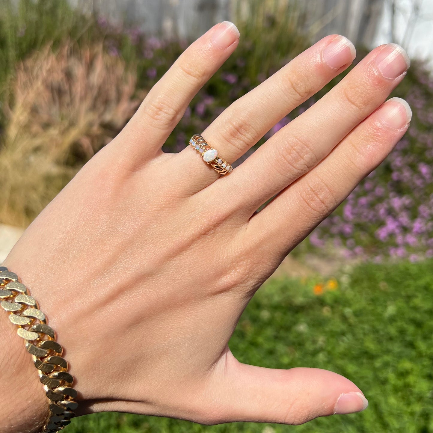 An Australian opal crisscross ring worn on a hand in the sunlight, shown against an outdoor background.