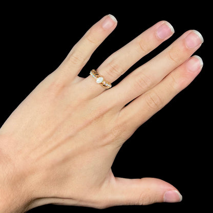 A gold crisscross ring set with Australian opals, worn on a hand that is held against a black background.