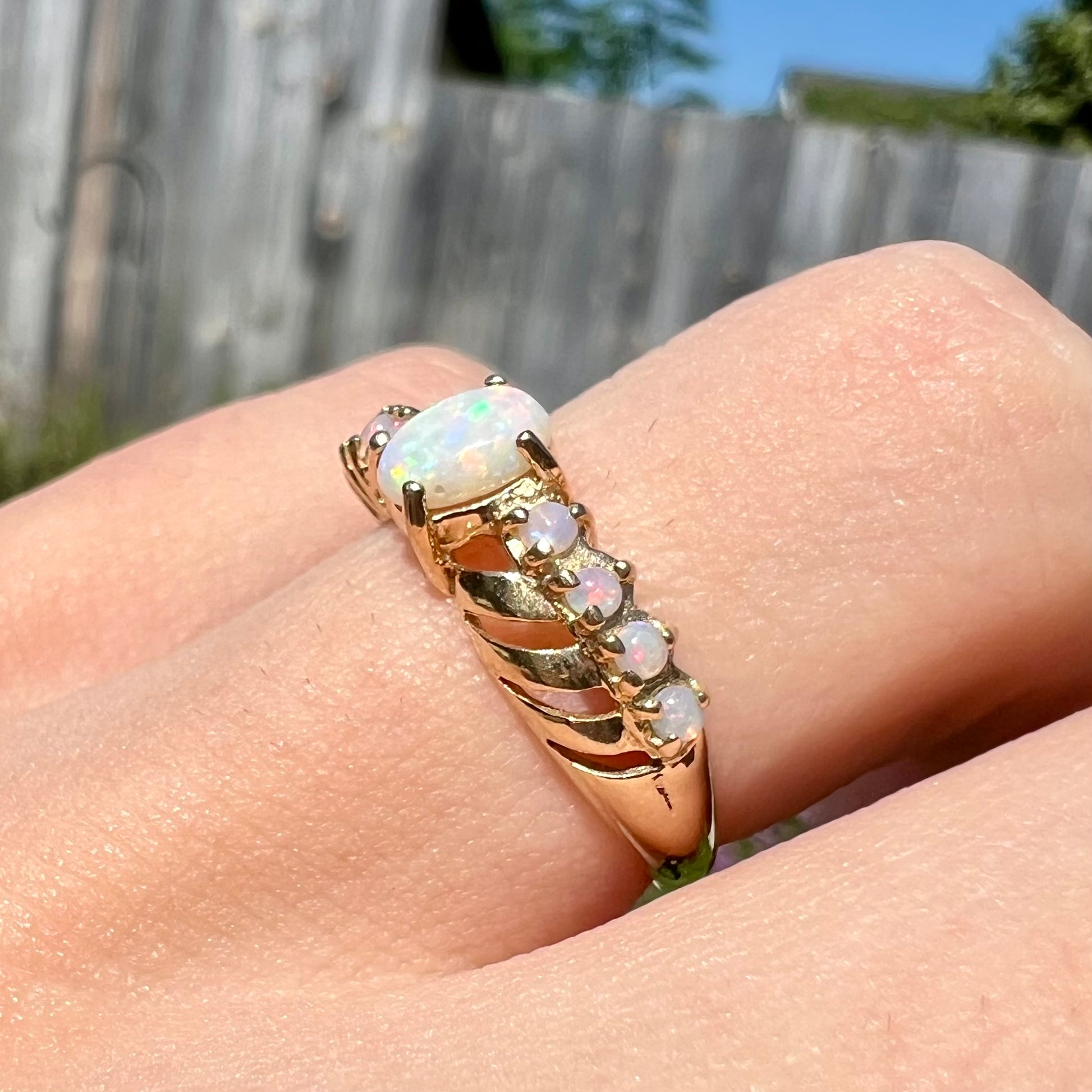 Angled close-up view of an Australian white opal crisscross ring worn on a finger in the sunlight.