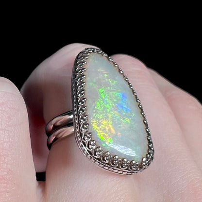 Macro view of an Australian opal ring in a sterling silver ring with a crown design, worn on a finger.  The opal has green, peacock-like fire.