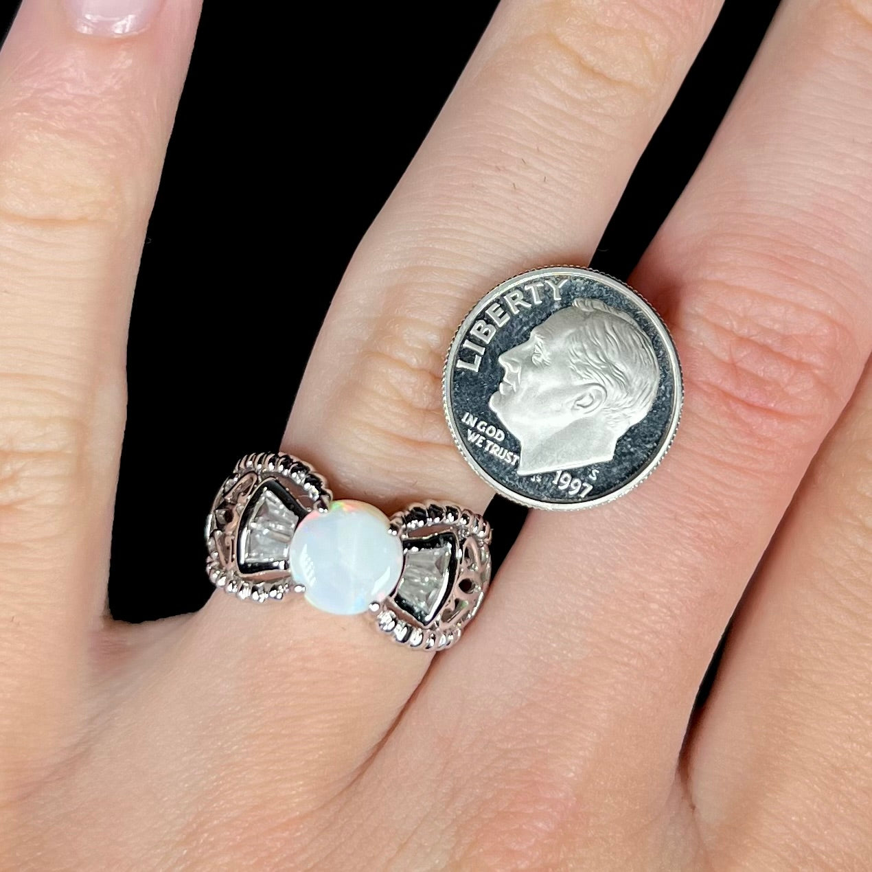 A round Australian white opal and CZ ring in white base metal worn next to a dime for scale.