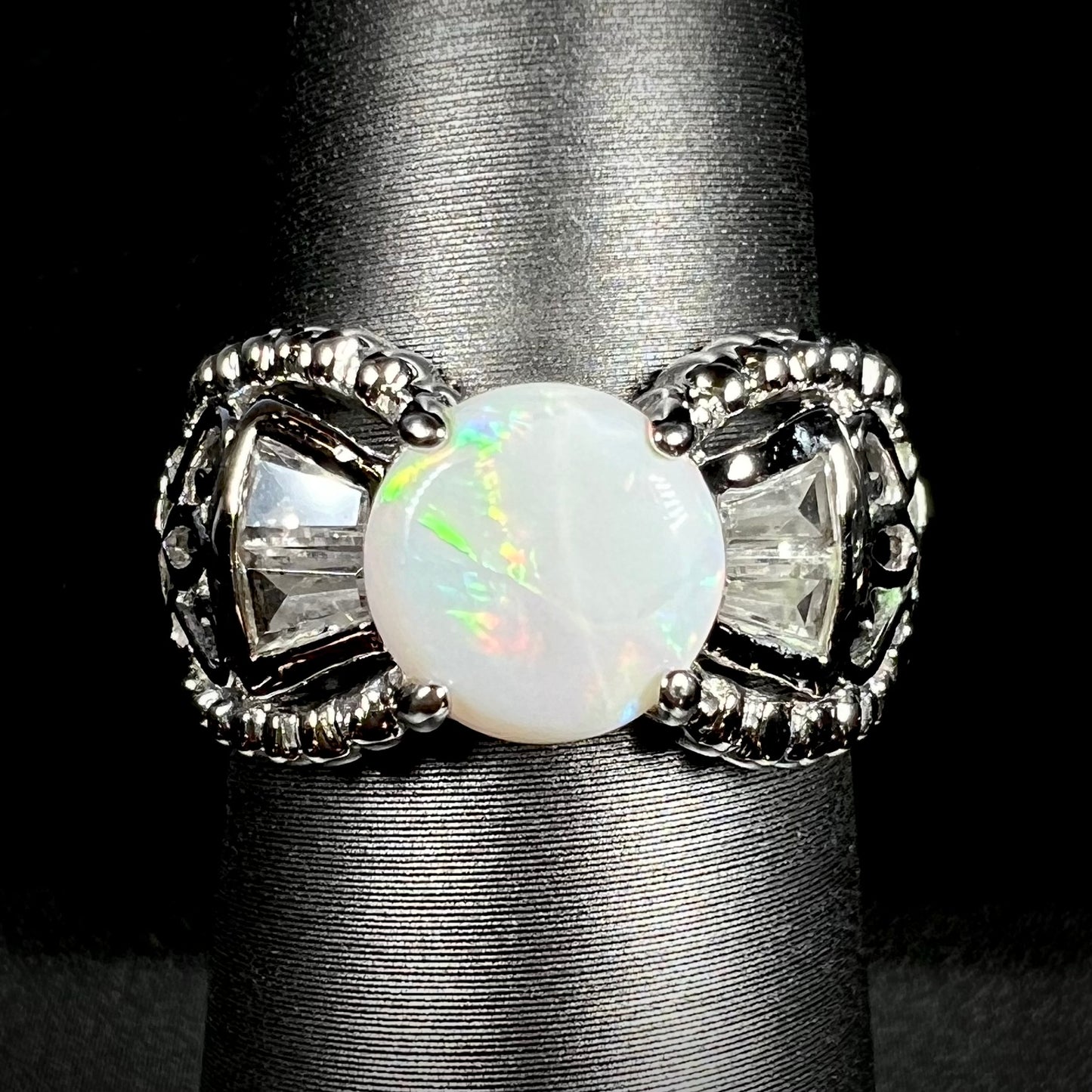 Front view of a round Australian white opal and CZ ring in white base metal. 