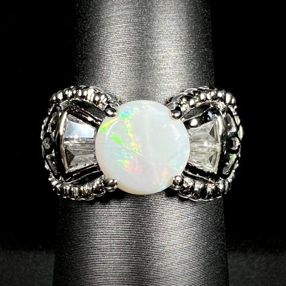 Front view of a round Australian white opal and CZ ring in white base metal. 