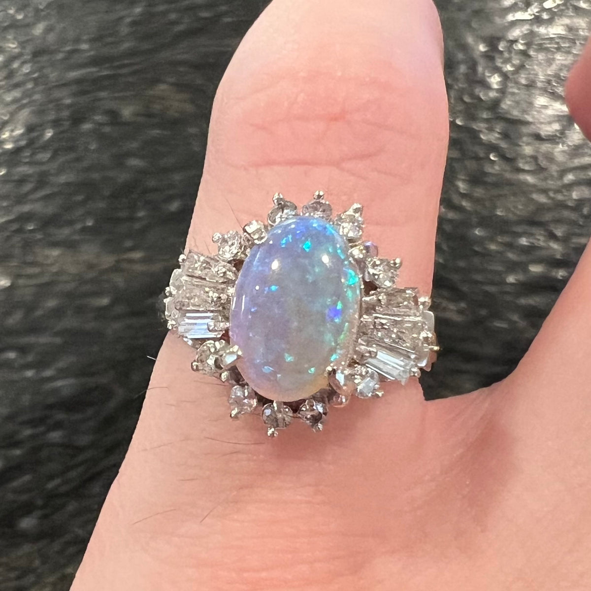 Highly-directional Australian semi-crystal opal ballerina ring shown on pinky finger straight-on in dim lighting; the opal has subdued blue color