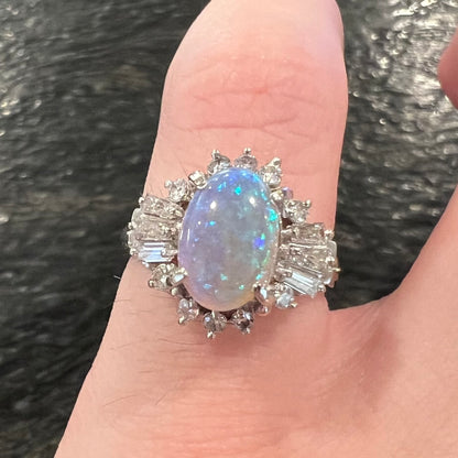 Highly-directional Australian semi-crystal opal ballerina ring shown on pinky finger straight-on in dim lighting; the opal has subdued blue color