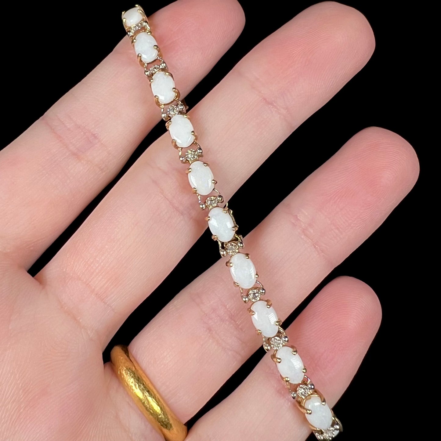 An estate opal and diamond tennis bracelet in 10k gold, held in a hand and shown from the front.