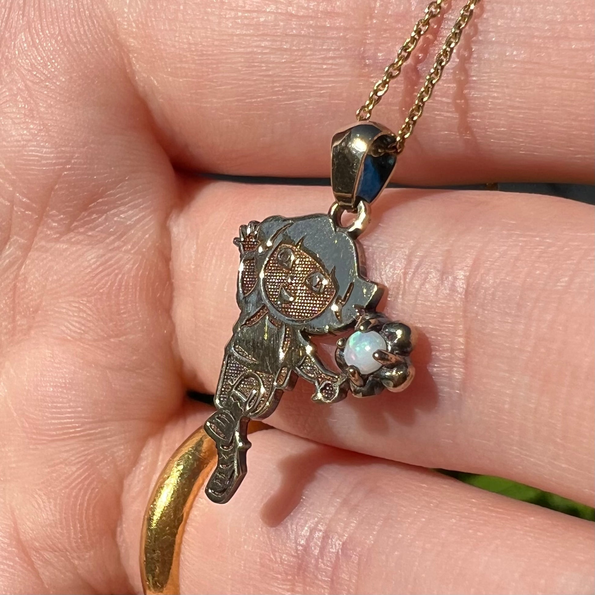 Round Australian opal Dora the Explorer pendant shown close-up in a hand held at an angle in natural light.  The opal has subtle green play of color.