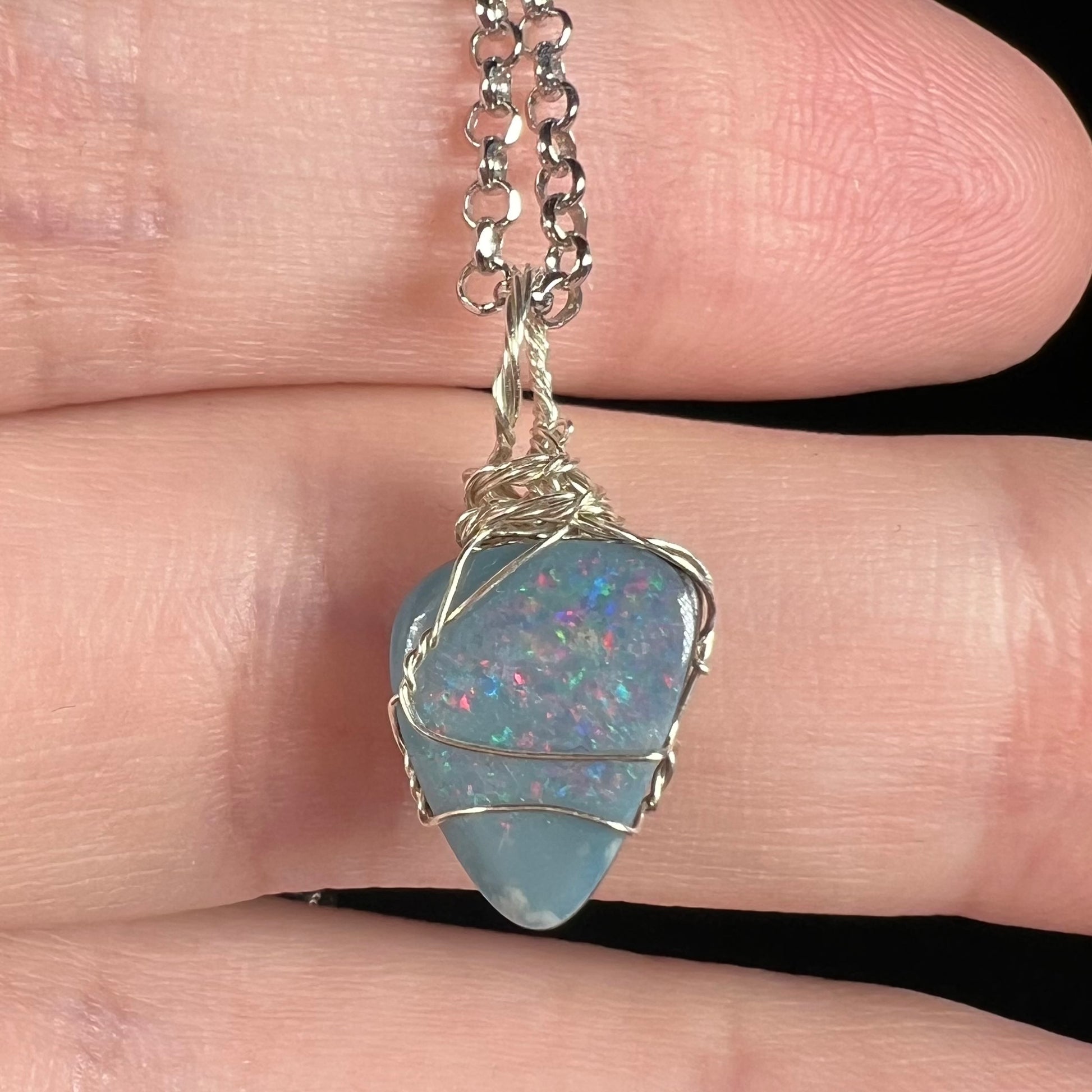 Close-up of an Australian opal doublet pendant with red and blue flashes of color, mounted in a delicate sterling silver wire wrapped setting.
