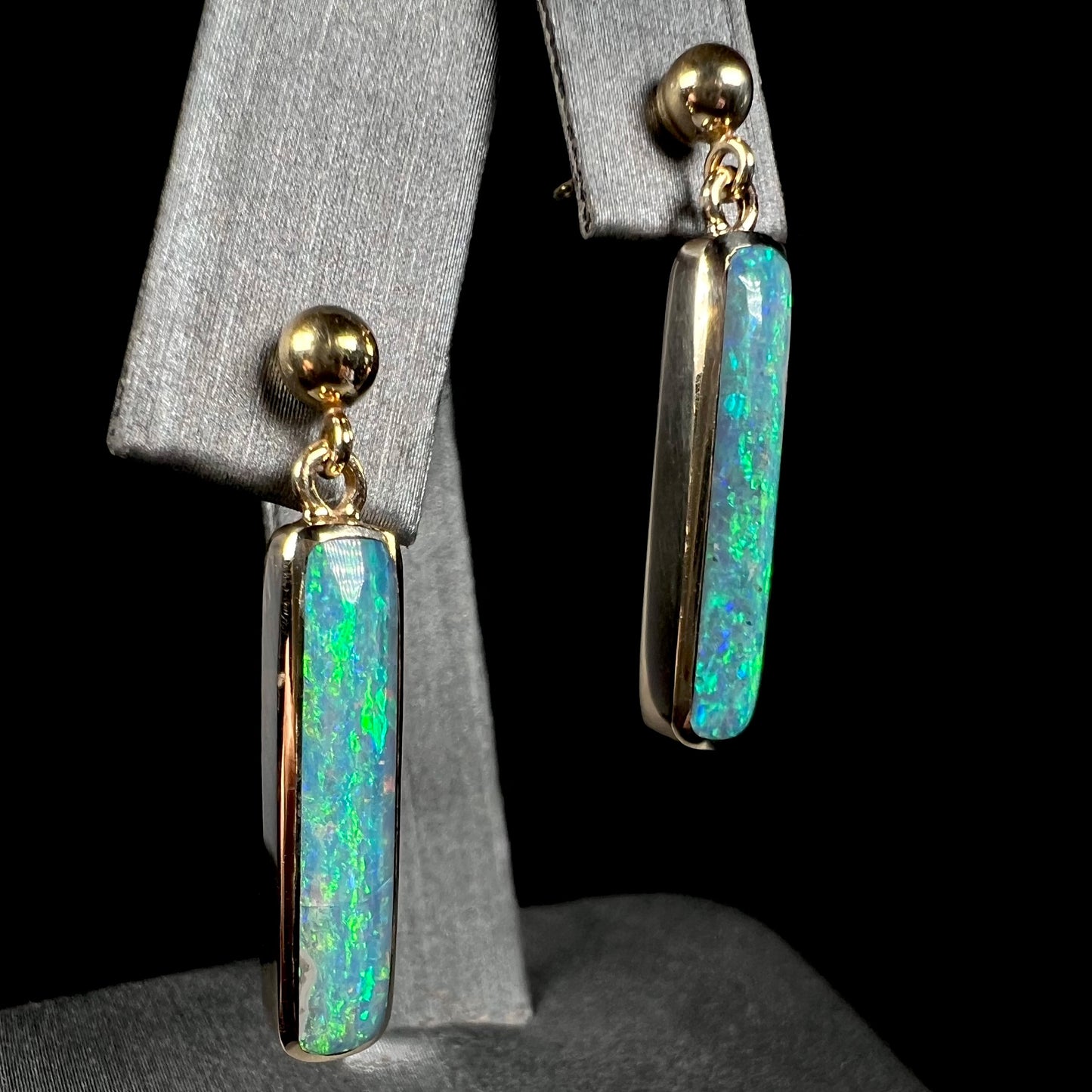 Angled view of gold Australian opal drop earrings against a black background.