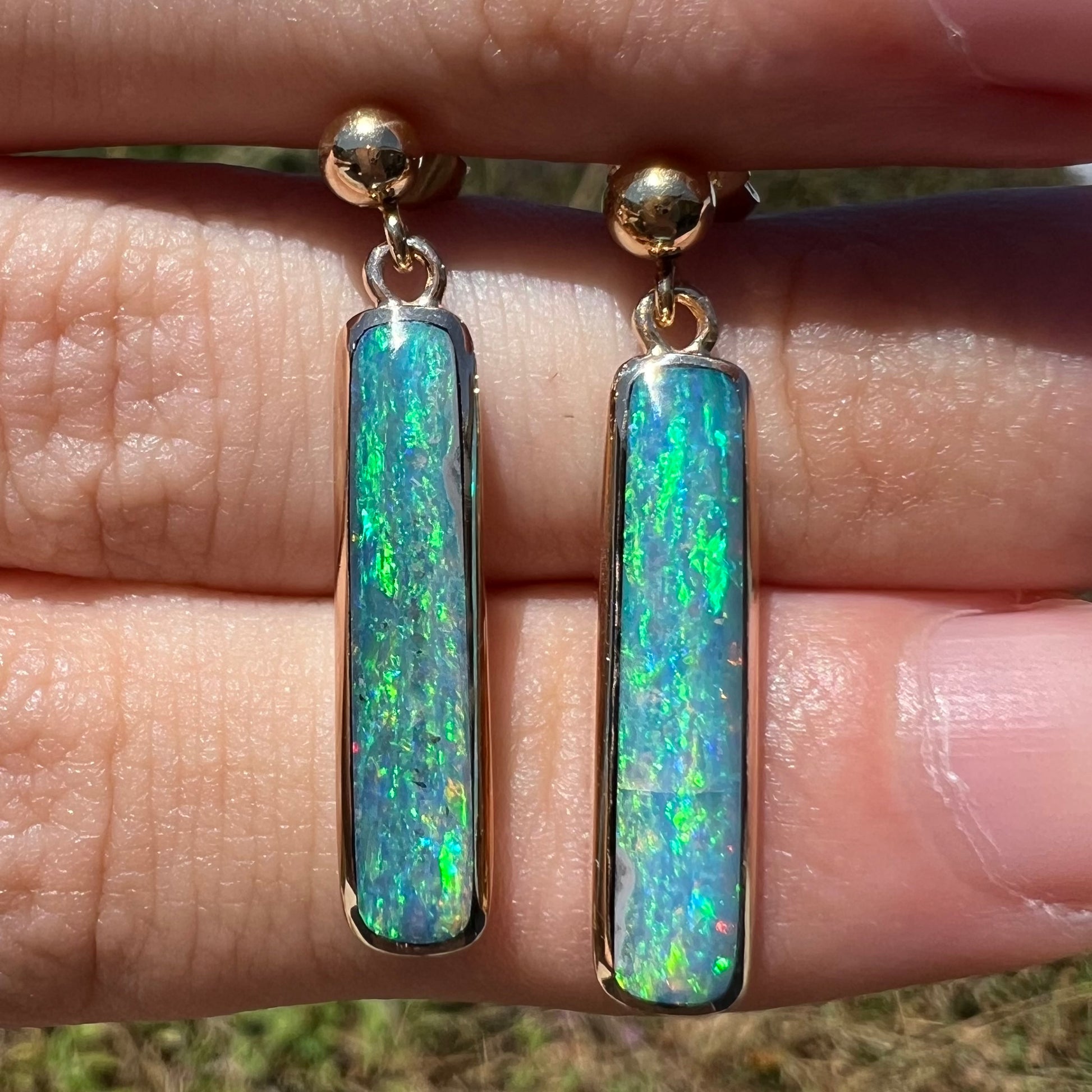 Close-up sunlit front view of a pair of Australian opal drop earrings in yellow gold.