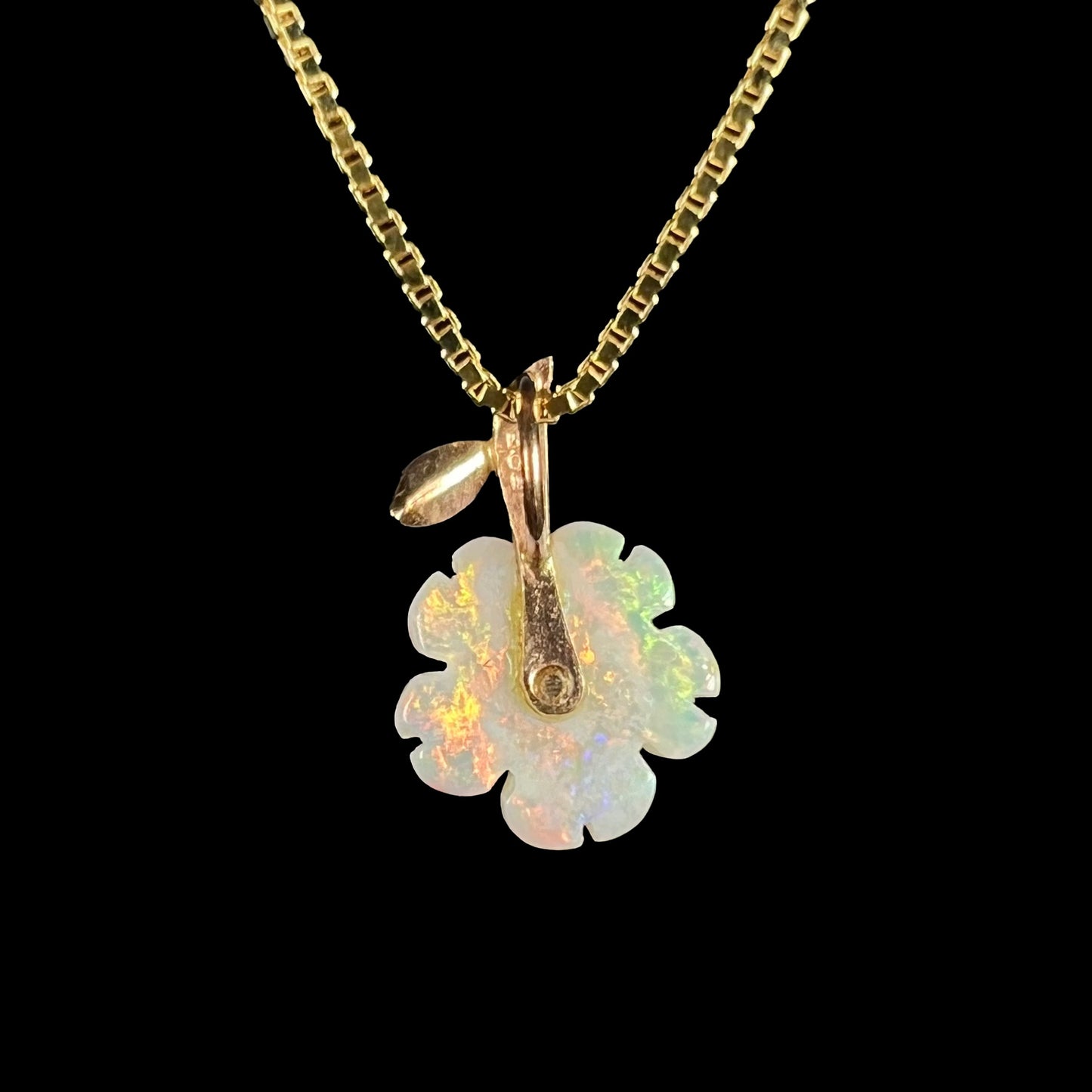 Back side of a pendant featuring an Australian opal flower carving, shown on a gold-tone box chain against a black background.