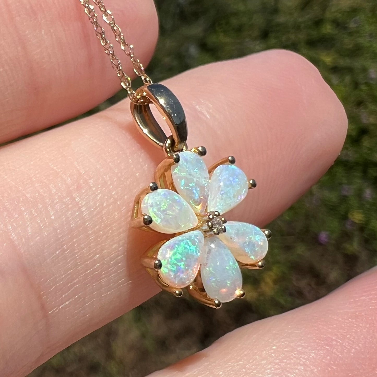Close-up of 10k gold Australian opal flower necklace on chain shown resting on fingers in sunlight