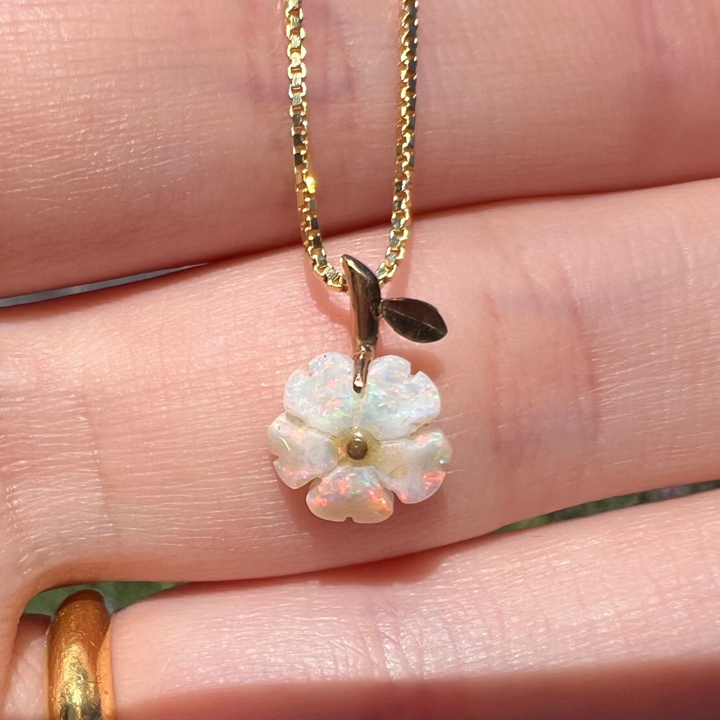 Close-up of an Australian opal flower pendant held in a hand in natural light.  The opal has pinkish red play of color.