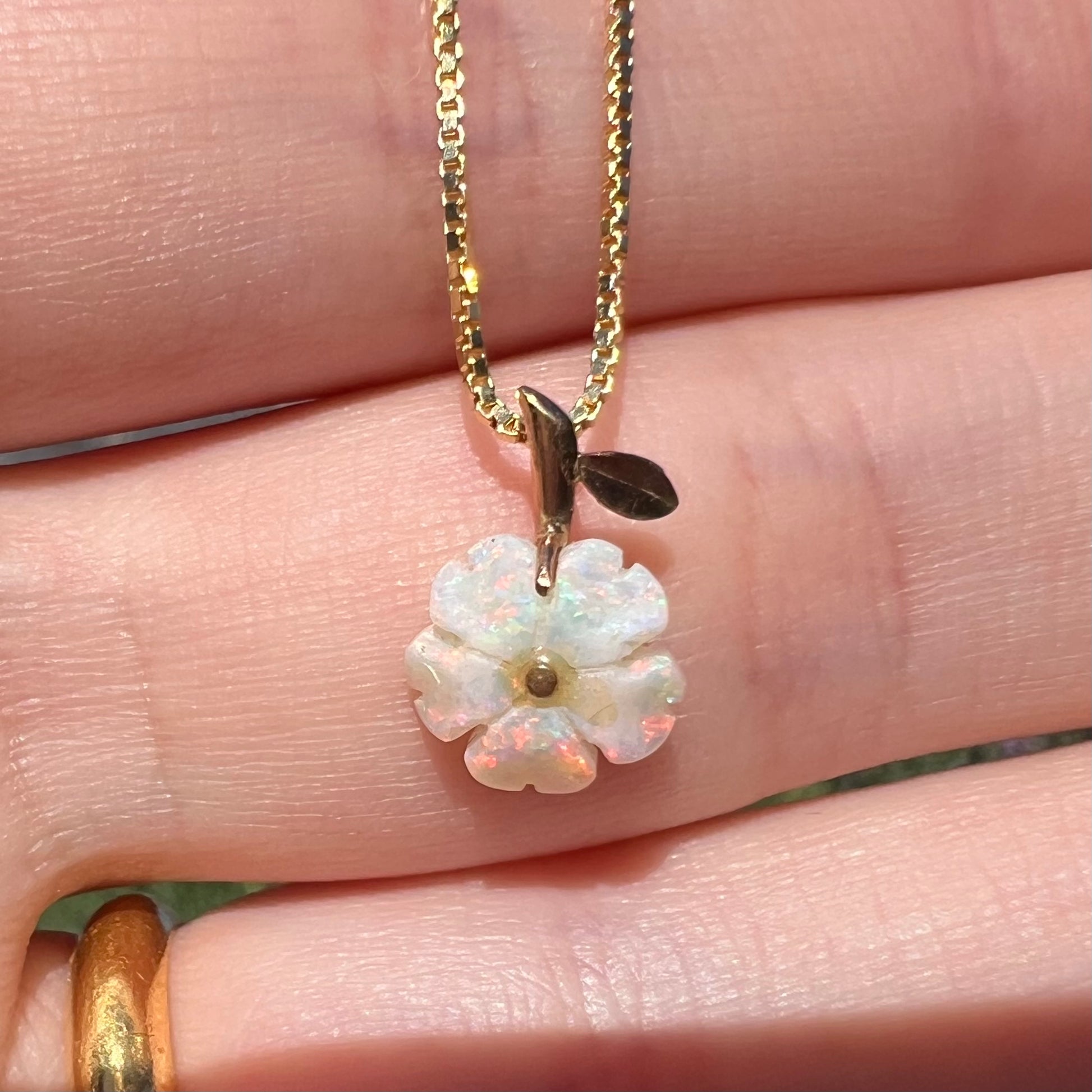 Close-up of an Australian opal flower pendant held in a hand in natural light.  The opal has pinkish red play of color.