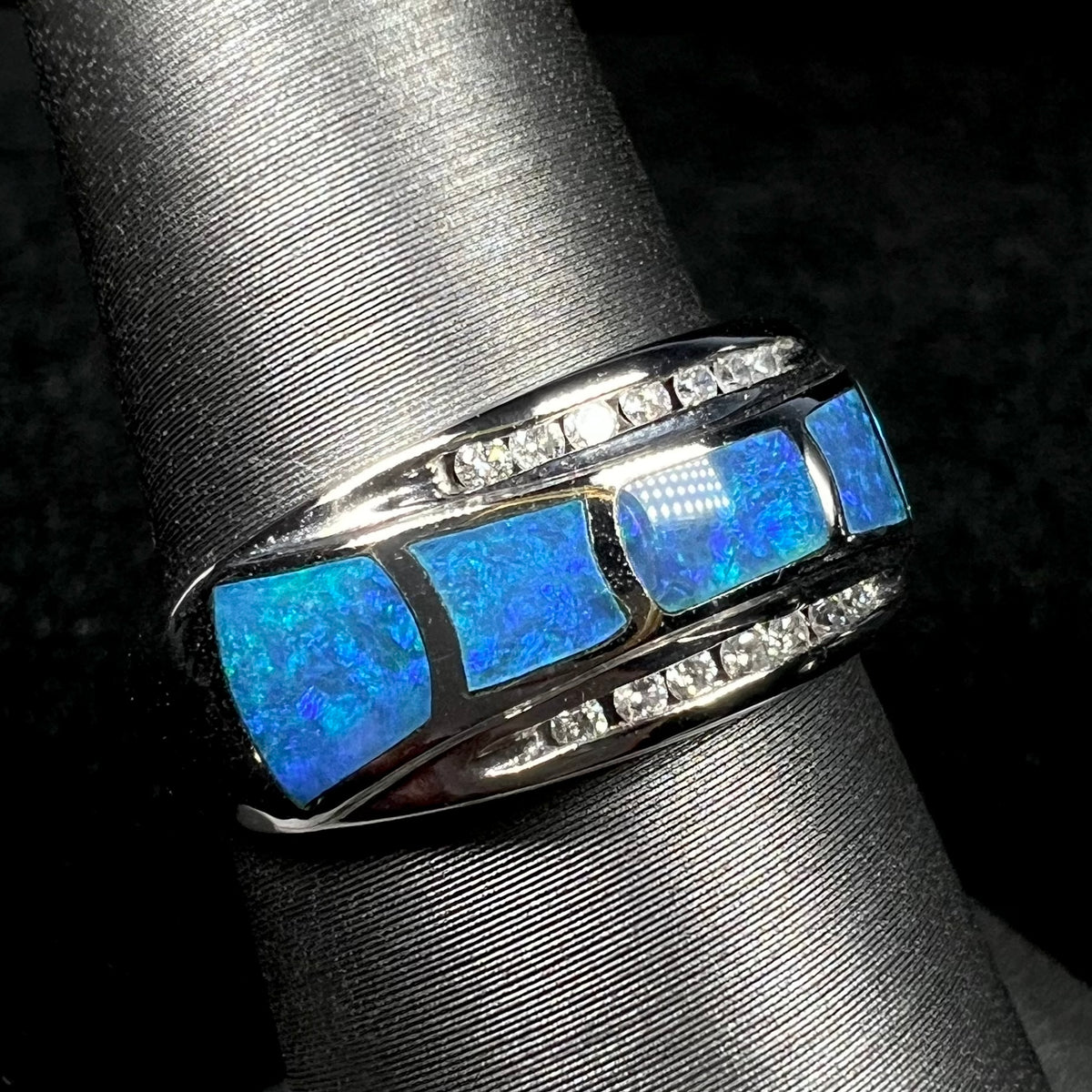 Unisex blue Australian opal inlay ring with channel-set diamond accents in 14k white gold shown close-up from angle on ring display