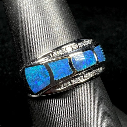 Unisex blue Australian opal inlay ring with channel-set diamond accents in 14k white gold shown close-up from angle on ring display