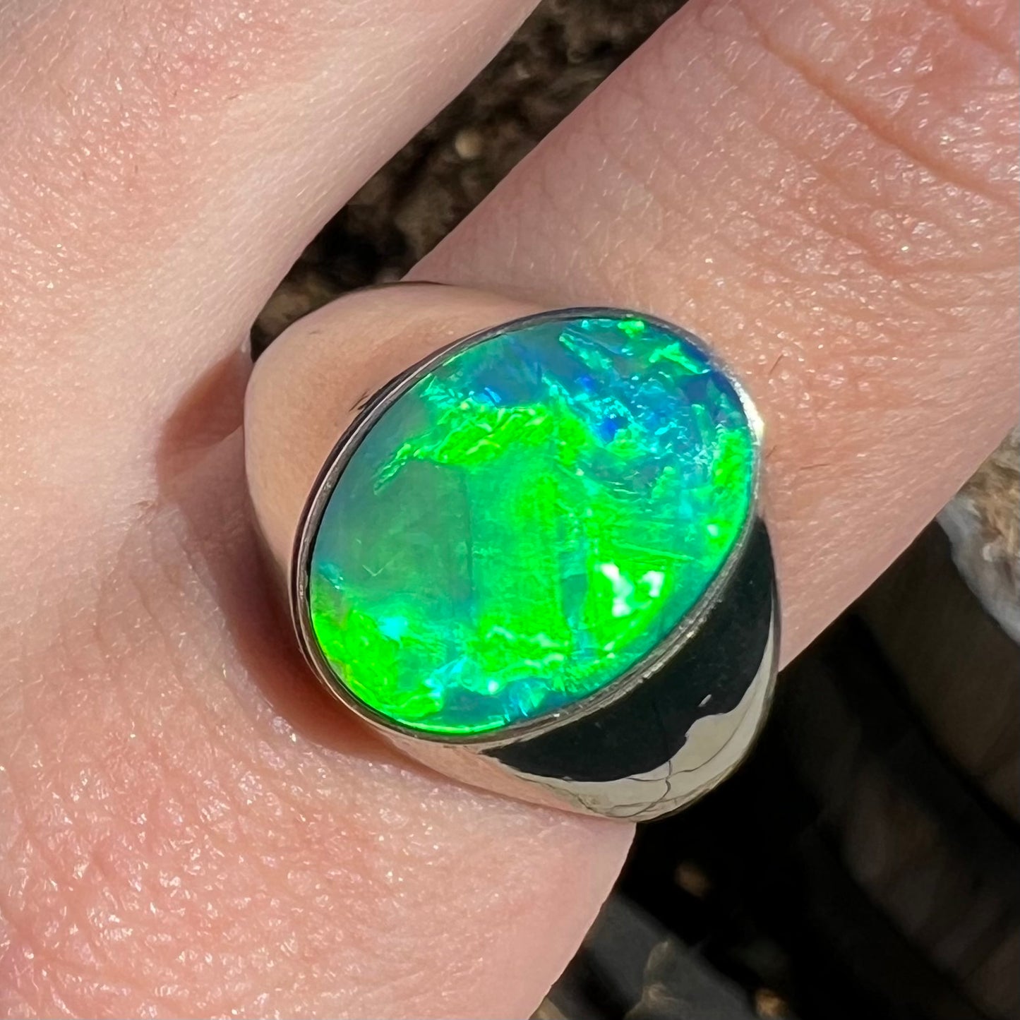 Close-up of Australian opal men's ring on finger.  Green flash is seen in natural sunlight