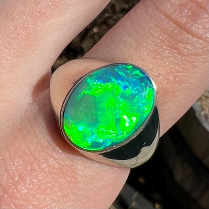 Close-up of Australian opal men's ring on finger.  Green flash is seen in natural sunlight