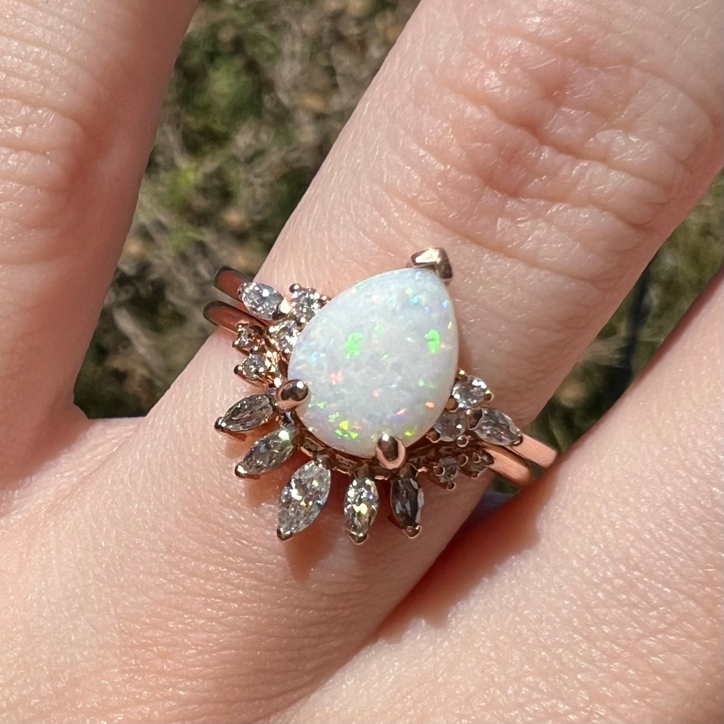 Close-up of Australian opal and moissanite-accented wedding ring set in rose gold, worn on finger under sunlight