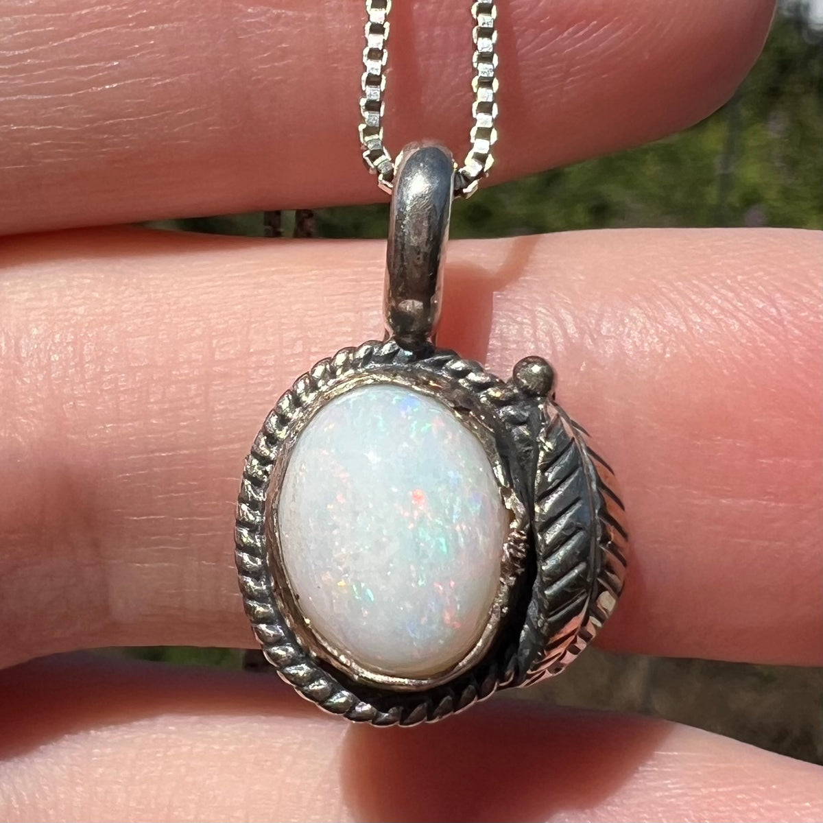 Close-up of handmade sterling silver Australian opal pendant with feather design, held in sunlight