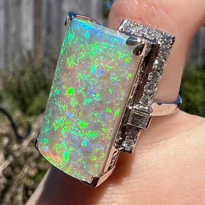 An N7 Australian light opal ring viewed on finger from angle in sunlight, green and blue play-of-color is seen throughout the entirety of its transluscent, smoky semi-crystal body.