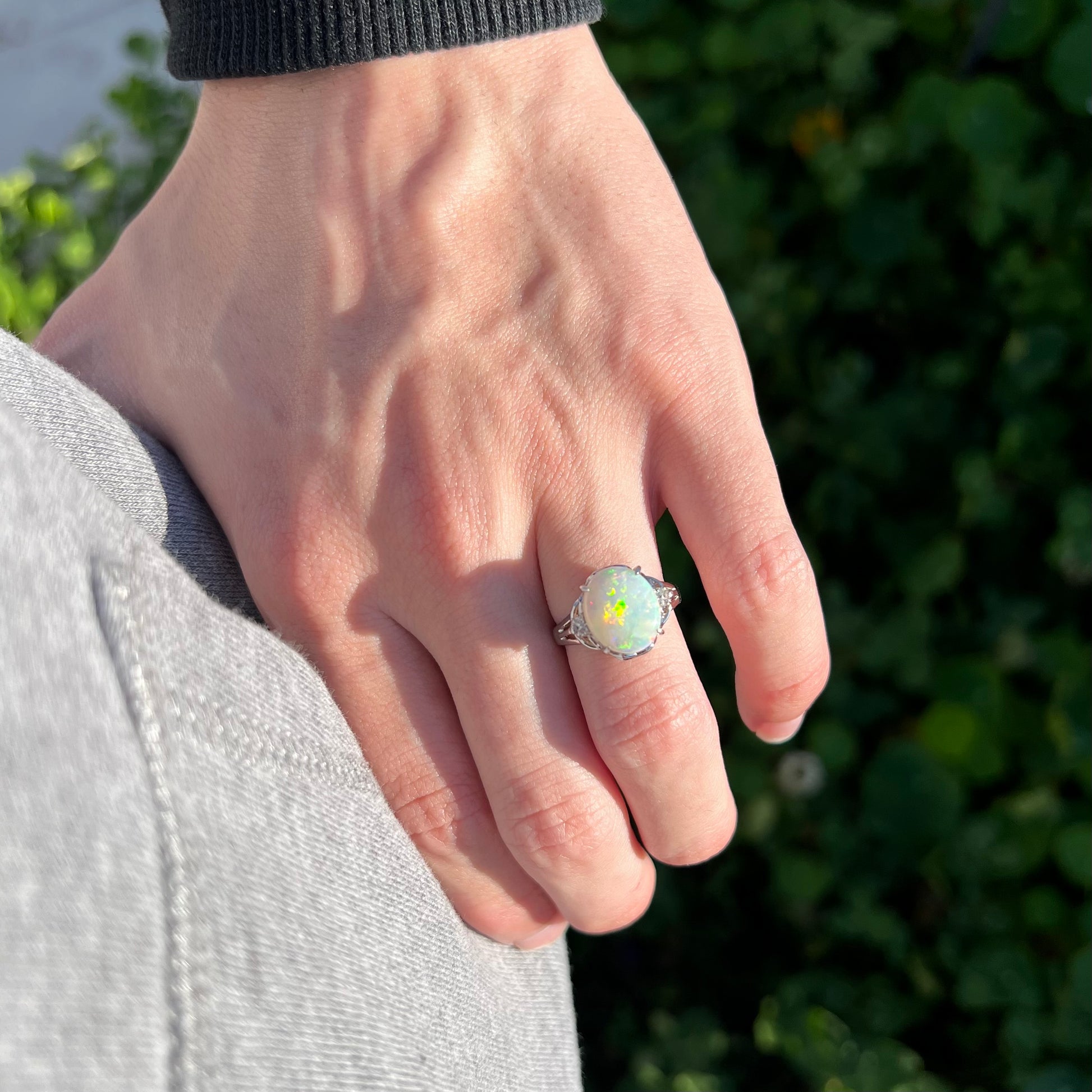 A platinum Australian opal ring with diamond accents, resting on a model's hand in the sun.