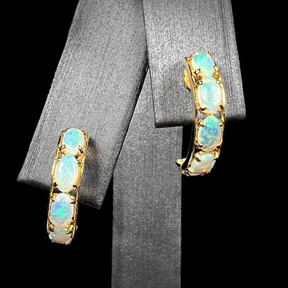 A pair of Australian crystal opal semi-hoop earrings in yellow gold shown on an earring display against a black background.