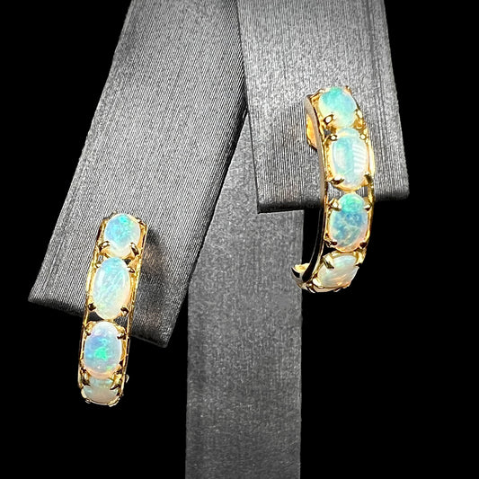 A pair of Australian crystal opal semi-hoop earrings in yellow gold shown on an earring display against a black background.