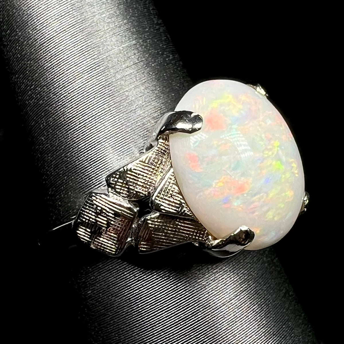 Prong-set Australian opal solitaire ring in texutred 14k white gold, shown close-up from angle on ring display