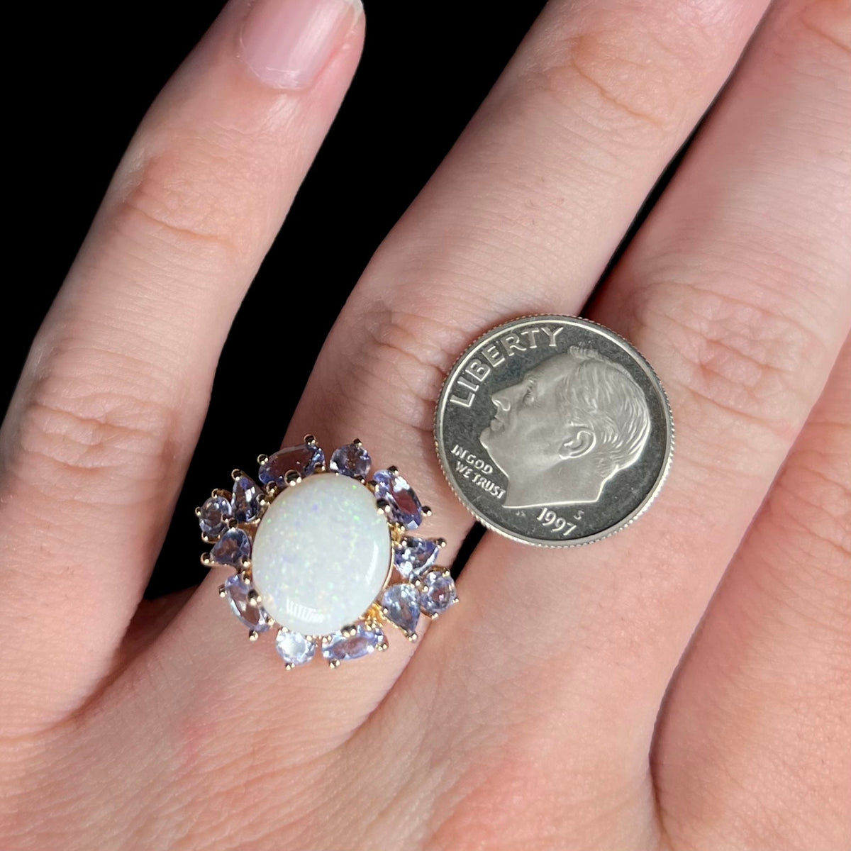 Close-up of hand wearing 14k gold Australian opal ring with cluster of tanzanite accents next to a US dime coin for scale