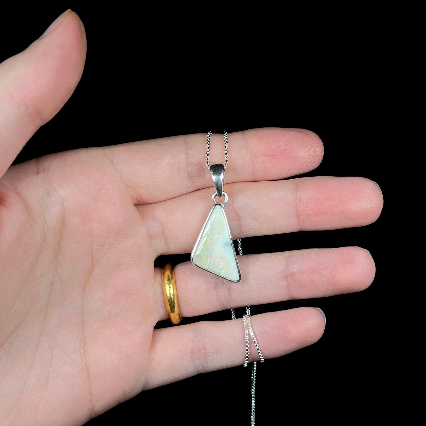 A white Australian boulder opal necklace in .950 silver, held in a hand against a black background.