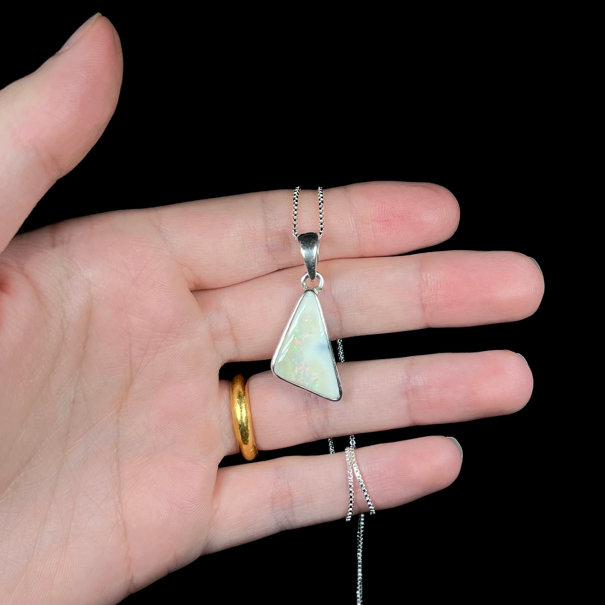 A white Australian boulder opal necklace in .950 silver, held in a hand against a black background.