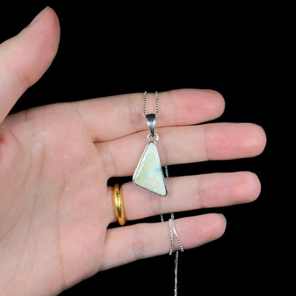 A white Australian boulder opal necklace in .950 silver, held in a hand against a black background.