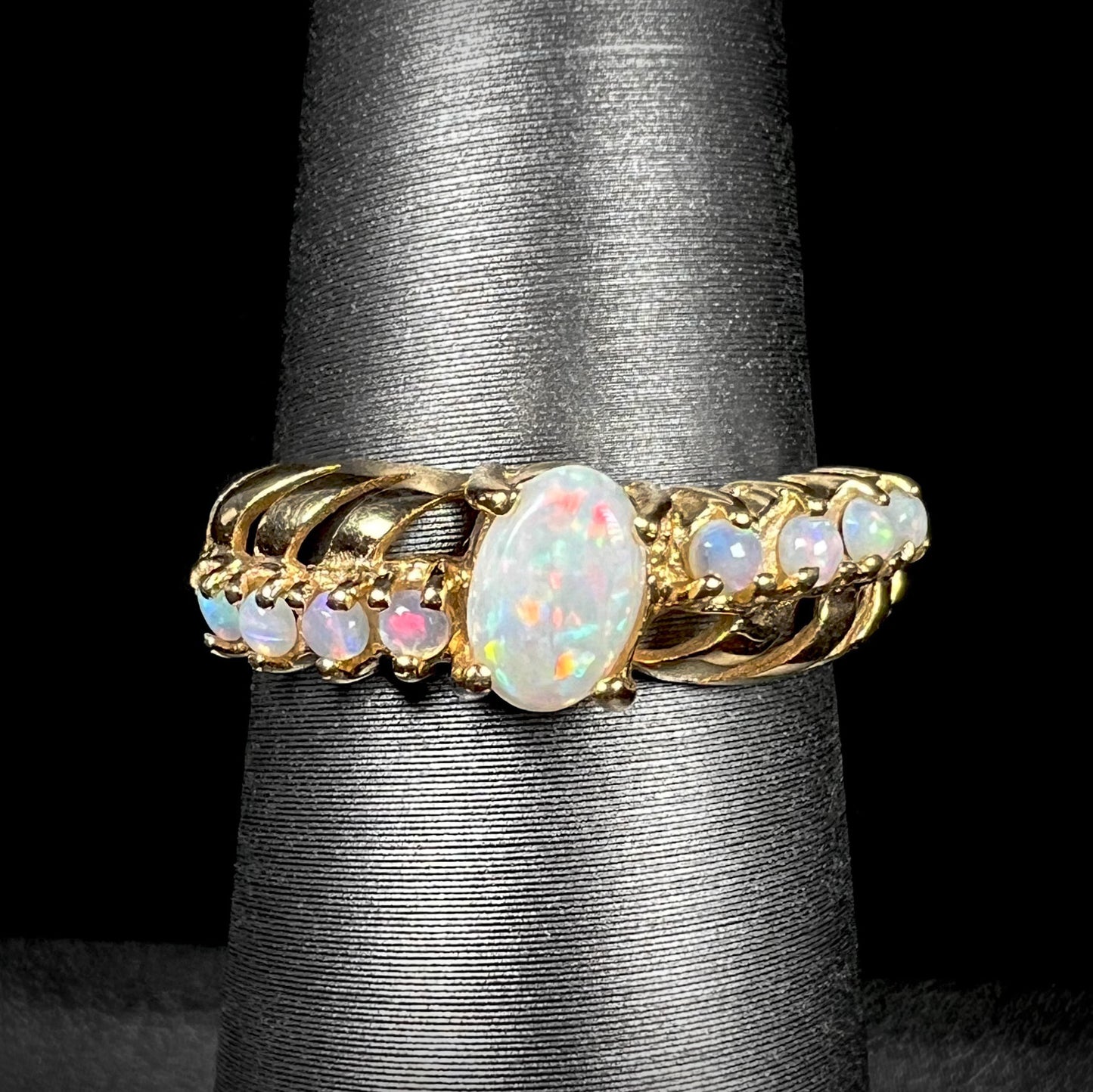 A yellow gold ring featuring two crossing, alternating lines of round cut Australian opals.  In the middle is a larger oval cut Australian opal.
