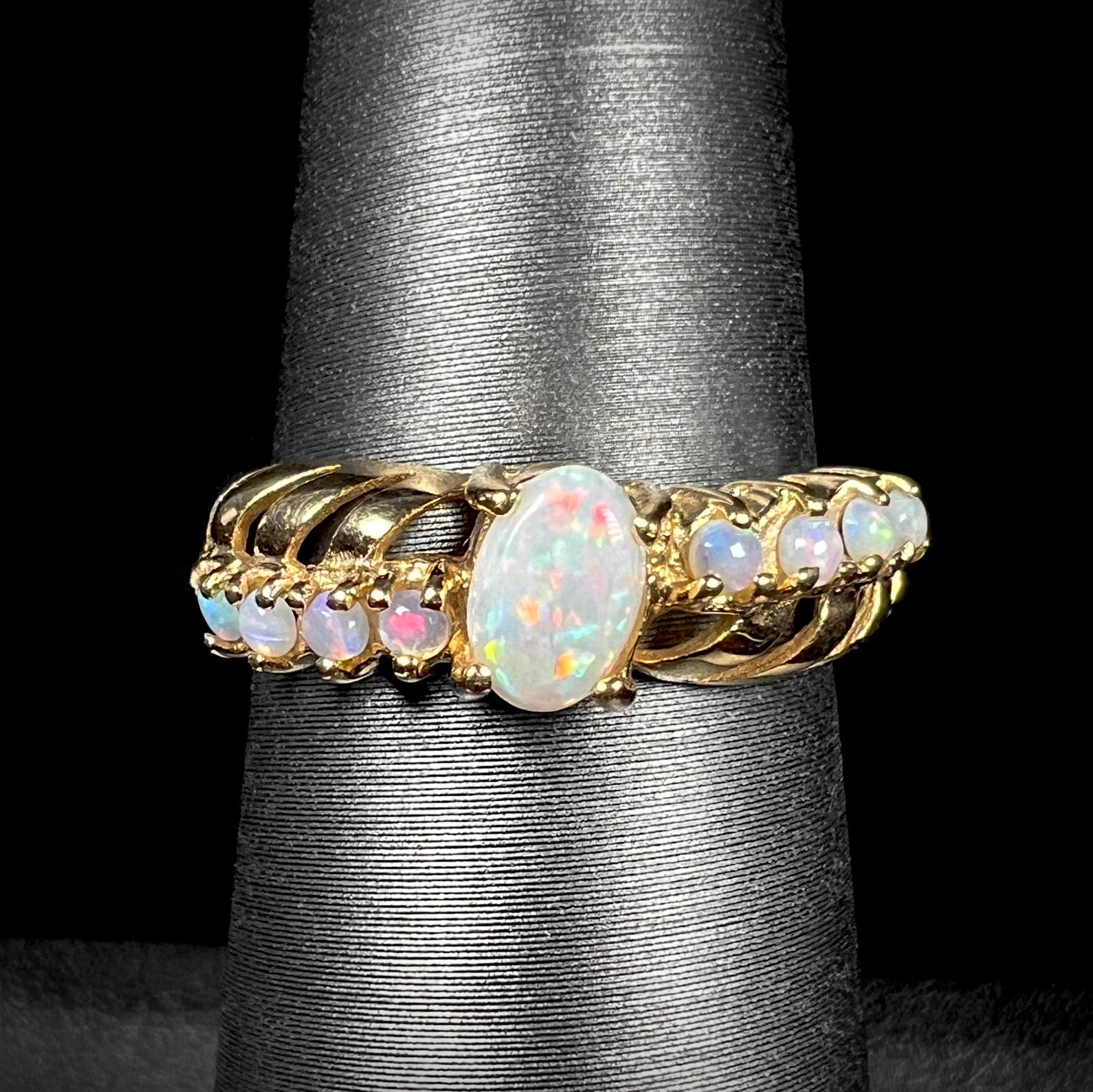 A yellow gold ring featuring two crossing, alternating lines of round cut Australian opals.  In the middle is a larger oval cut Australian opal.